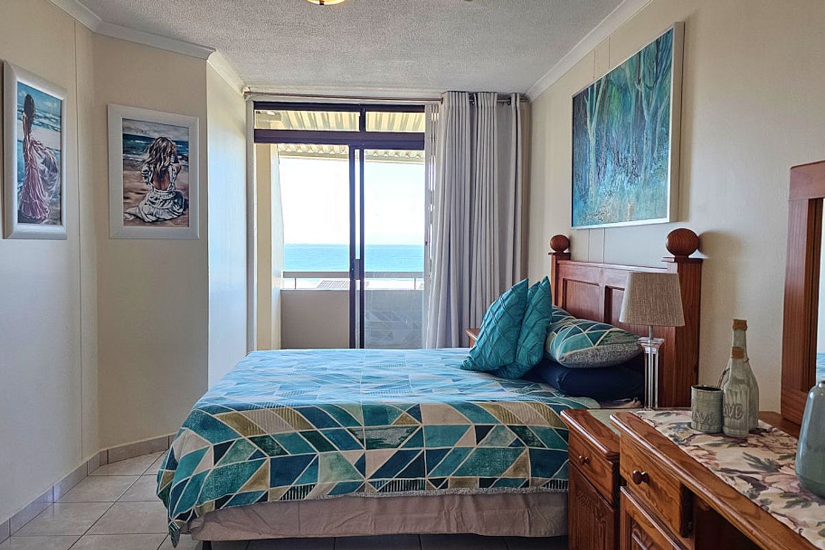 A bedroom featuring tiled flooring and a sliding glass door that opens onto a balcony with ocean views.