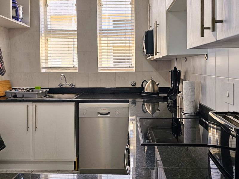 A functional kitchen featuring granite countertops, built-in cabinetry, a stainless steel sink, and an integrated electric hob with tiled backsplash.