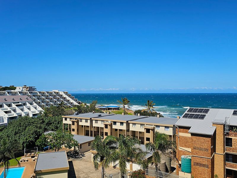 Elevated coastal view overlooking the apartment complex, swimming pool, and the ocean horizon.