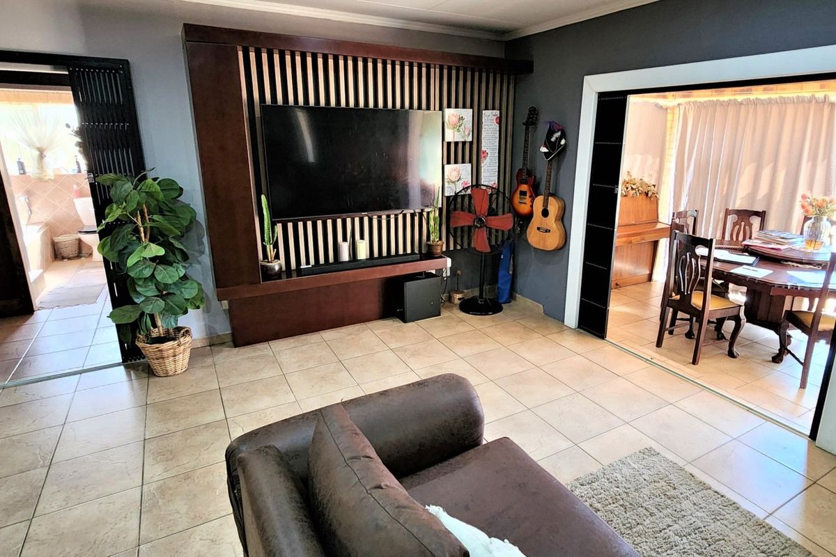 A living room featuring a custom built-in media wall with vertical timber slats, tiled flooring, and direct access to an adjacent dining area.