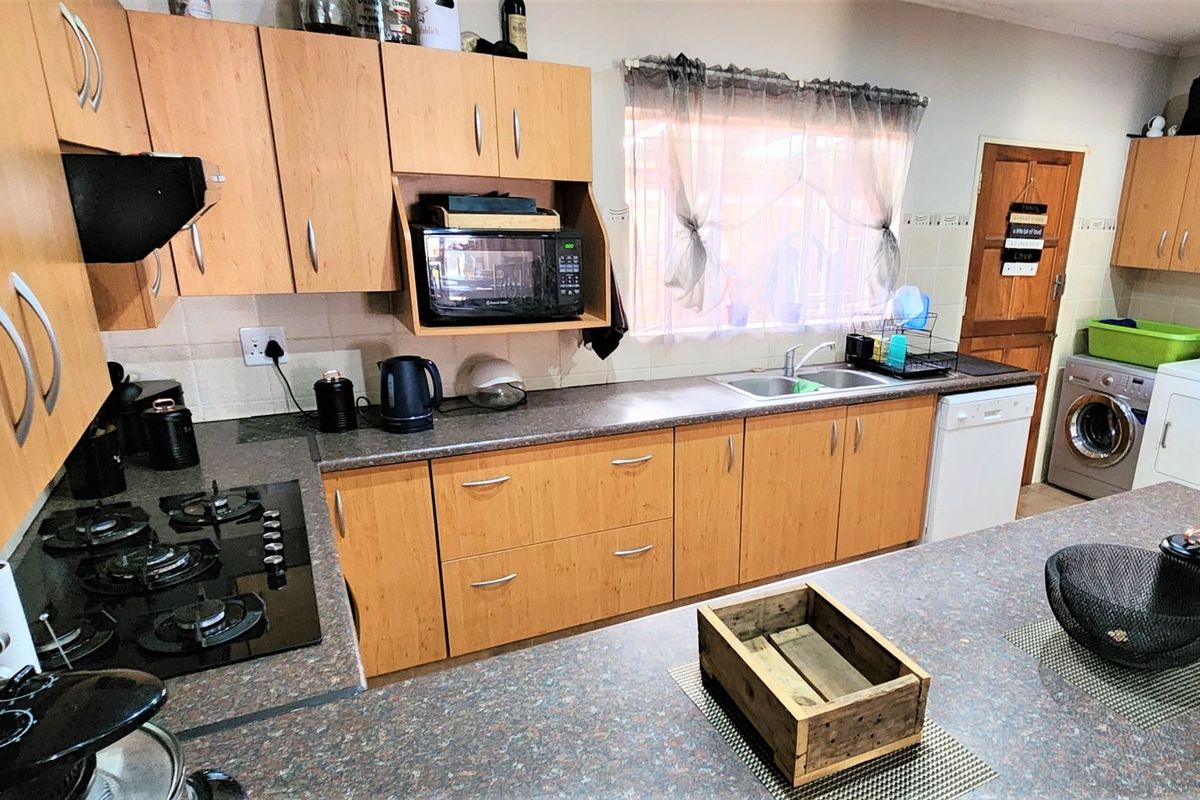 Functional kitchen featuring light wood-finish cabinetry, dark laminate countertops, a gas hob, and dedicated space for laundry appliances.
