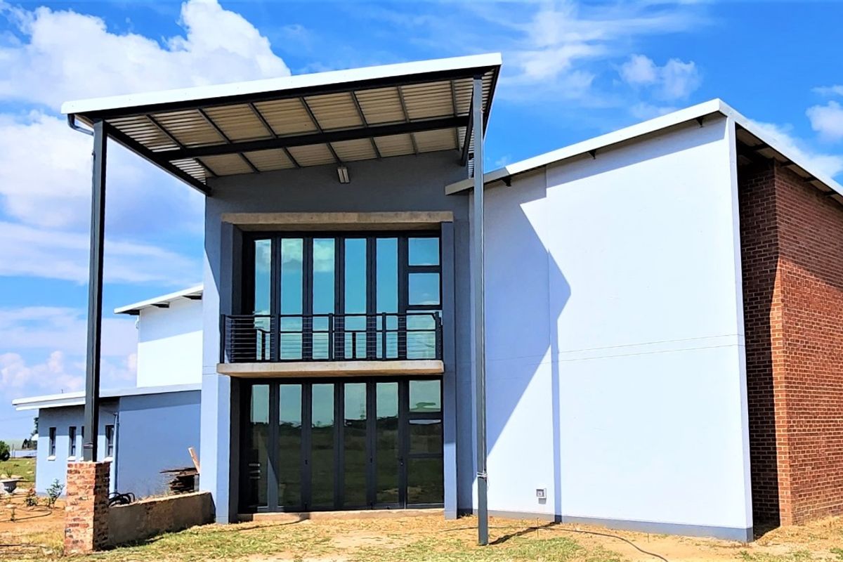 Rear elevation of a modern townhouse featuring a covered patio, upper-level balcony, and large aluminium-framed glass doors with a mix of brick and rendered finishes.