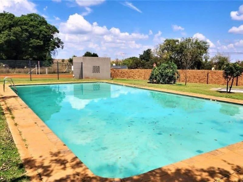 Outdoor swimming pool area featuring a rectangular pool with a ladder, surrounded by a lawn and brick boundary wall.
