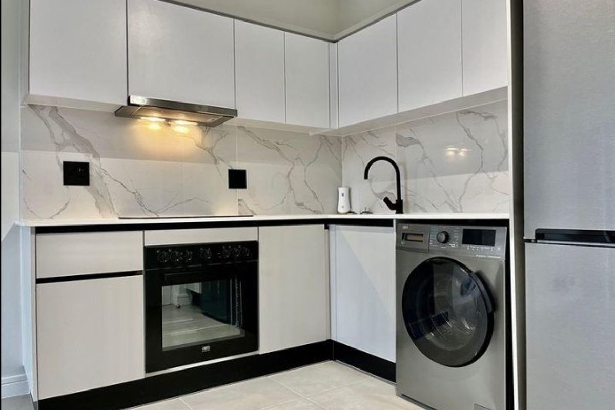 Modern kitchen featuring white cabinetry, marble-look splashback, stone countertops, built-in oven, extractor fan, and integrated laundry appliance space.