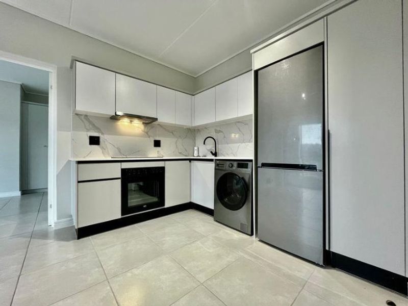 Modern kitchen featuring sleek white cabinetry, marble-look splashback, integrated oven, extractor fan, and tiled flooring in a clean, contemporary layout.