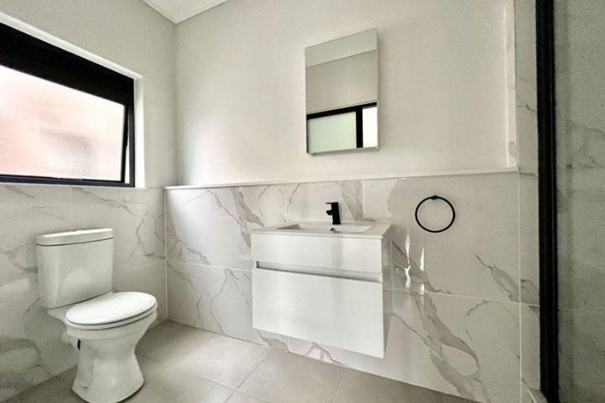 Modern bathroom featuring a wall-mounted vanity, marble-look wall tiling, black fixtures, and a clean, contemporary aesthetic.