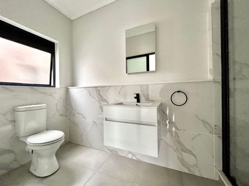 Modern bathroom featuring a wall-mounted vanity, marble-look wall tiling, black fixtures, and a clean, contemporary aesthetic.