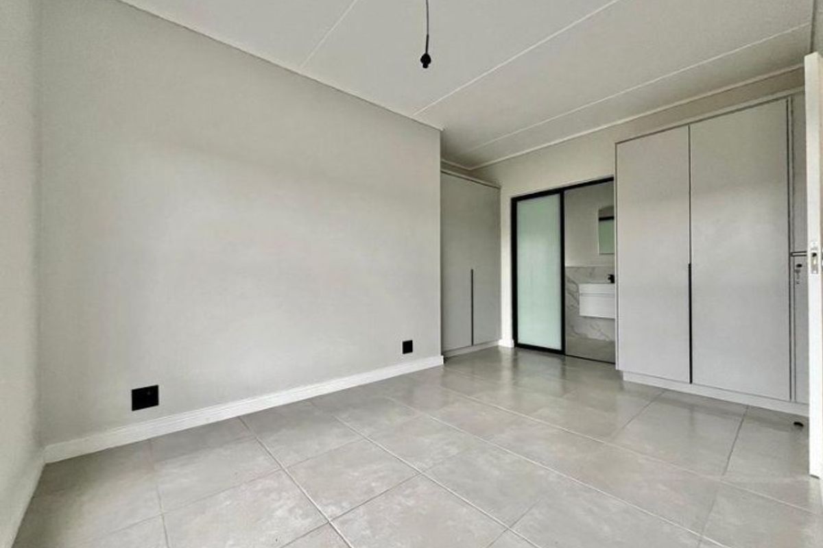 A bright, empty bedroom featuring neutral tiled flooring, built-in cupboards, and a sliding door leading to an en-suite bathroom.