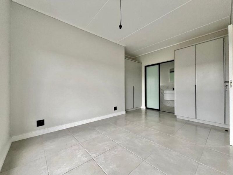 A bright, empty bedroom featuring neutral tiled flooring, built-in cupboards, and a sliding door leading to an en-suite bathroom.