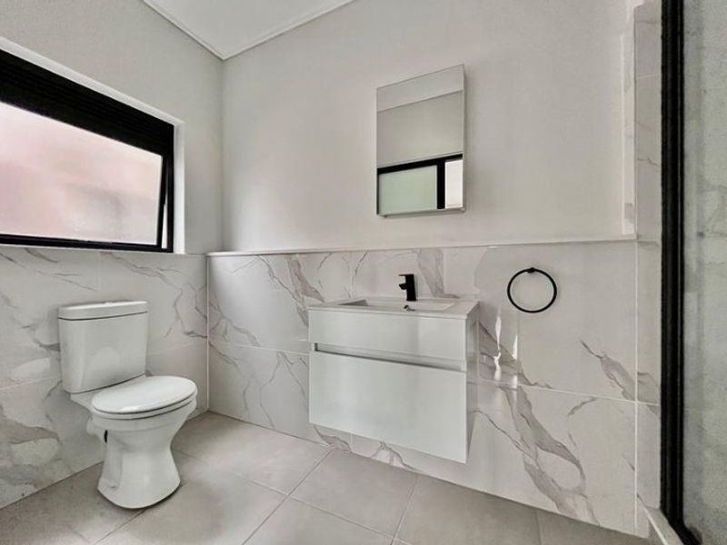 Modern bathroom featuring marble-look wall tiles, a sleek wall-mounted vanity with black tapware, and a contemporary toilet.