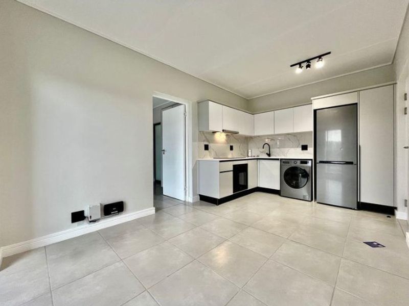Modern, minimalist kitchen featuring sleek white cabinetry, integrated appliances, stone-look backsplash, and neutral tiled flooring in an open-plan layout.