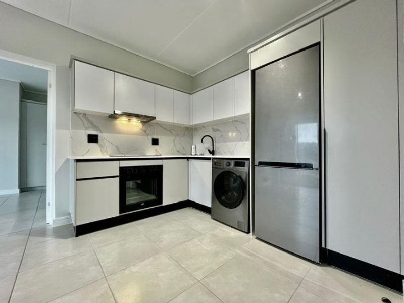 Modern kitchen featuring sleek white cabinetry, marble-look splashback, integrated oven, extractor fan, and tiled flooring in a clean, contemporary layout.