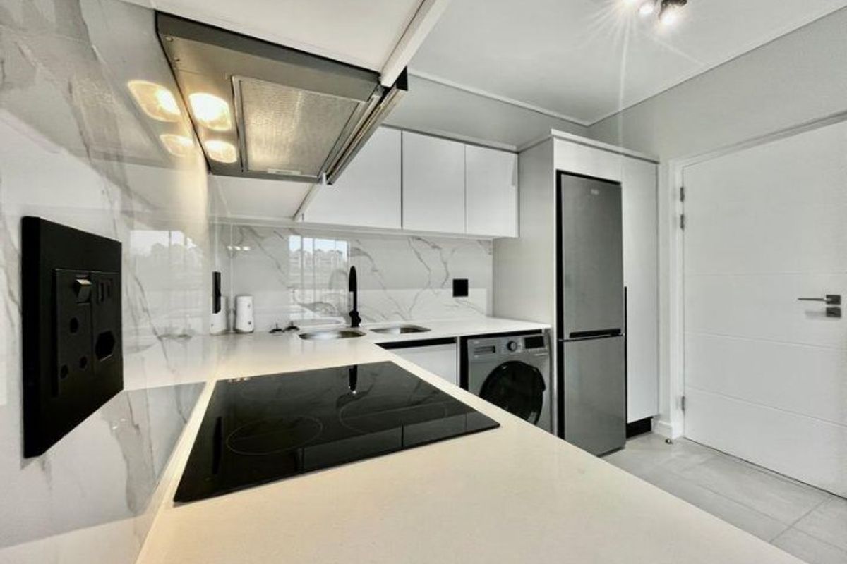 Modern kitchen featuring sleek white cabinetry, marble-look splashback, stone countertops, integrated appliances, and high-quality finishes throughout.