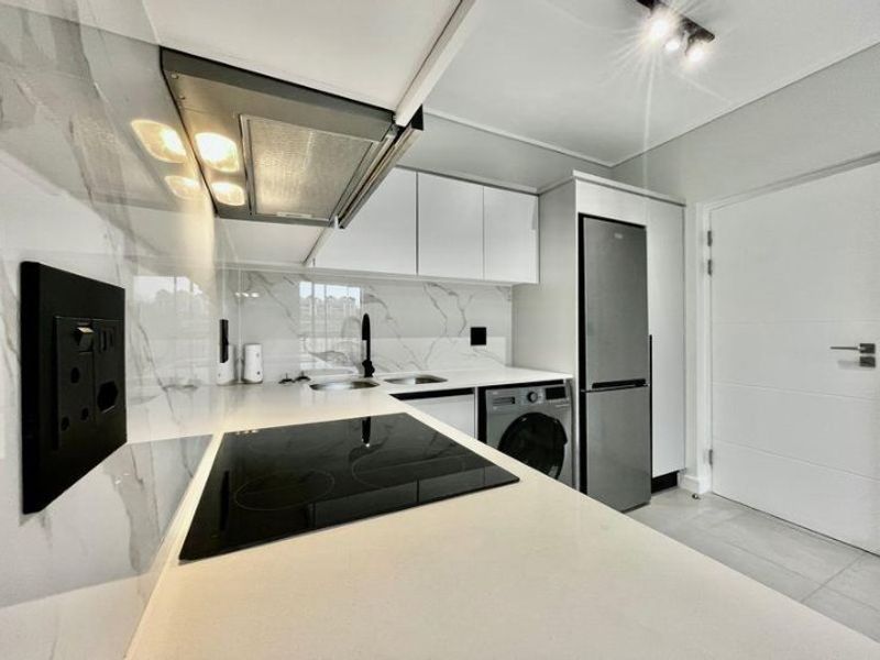 Modern kitchen featuring sleek white cabinetry, marble-look splashback, stone countertops, integrated appliances, and high-quality finishes throughout.