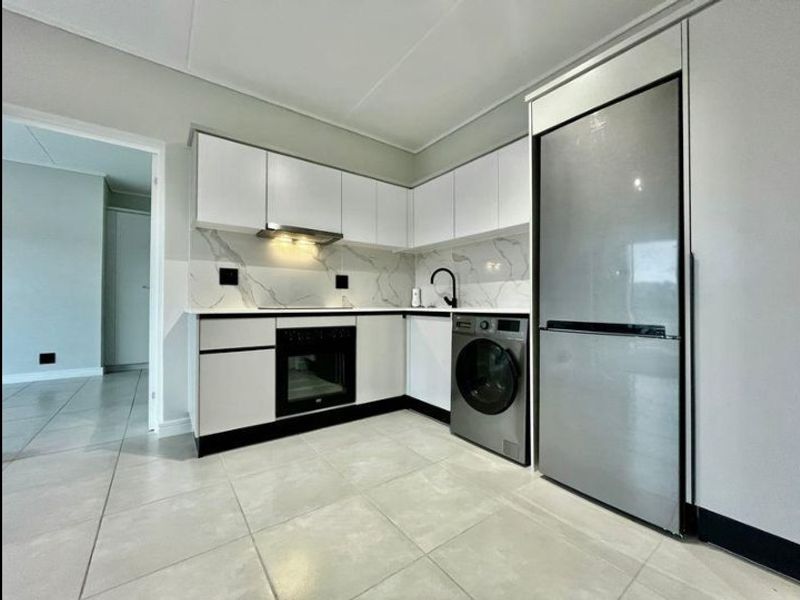 Modern kitchen featuring sleek white cabinetry, marble-look backsplash, integrated appliances, and neutral floor tiling in a clean, contemporary apartment setting.