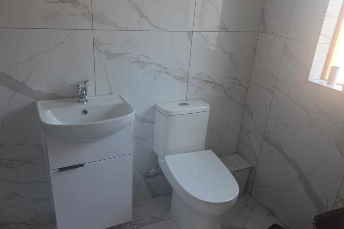 A modern bathroom featuring marble-look wall tiles, a sleek vanity basin, and a contemporary toilet.
