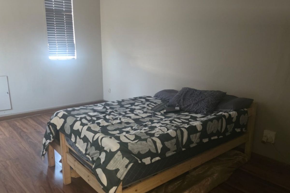 A simple bedroom featuring laminate flooring and a window with venetian blinds.