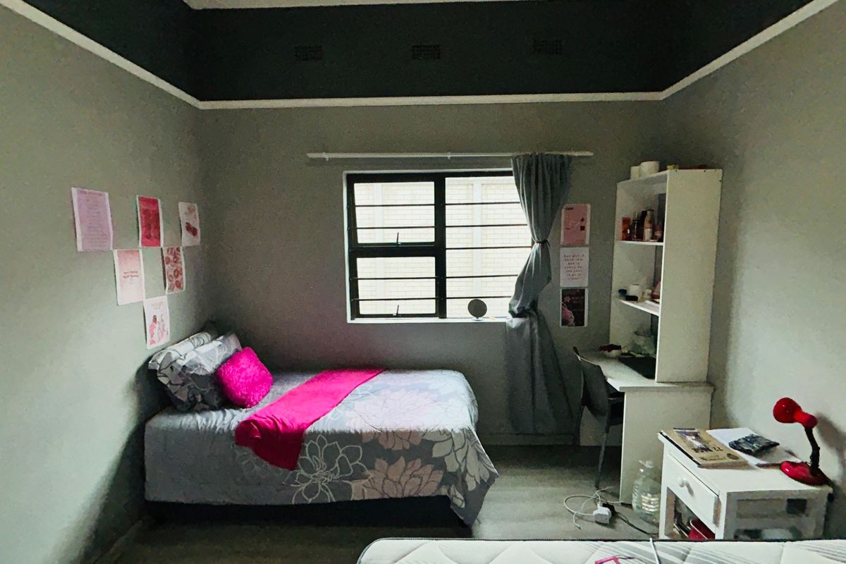 A functional bedroom featuring a window with security burglar bars, a built-in desk, and integrated shelving unit.