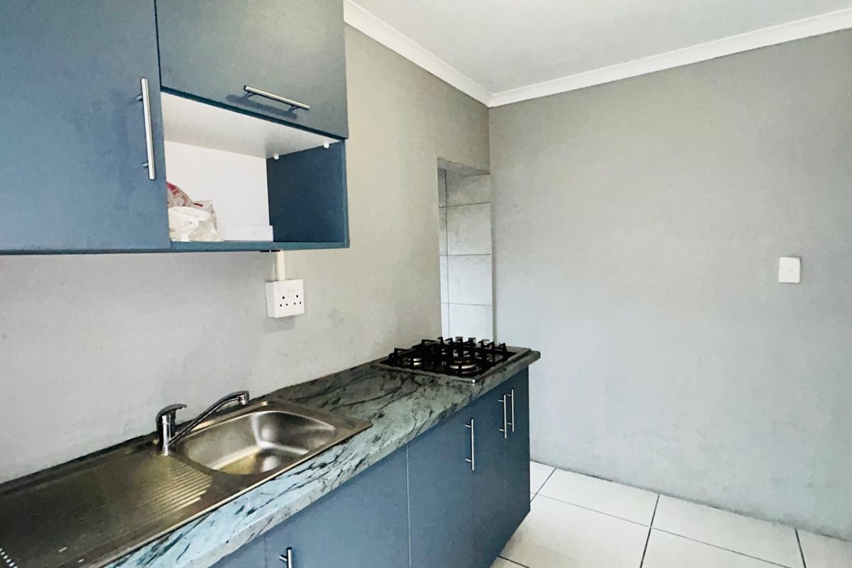 A compact kitchen featuring blue built-in cabinetry, a stone countertop with an integrated sink, a gas hob, and tiled flooring.