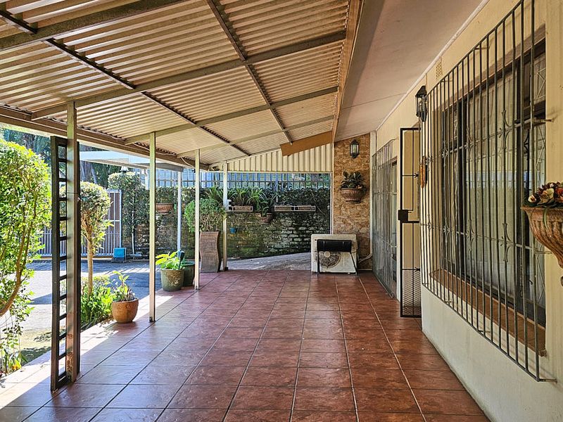 A covered outdoor patio area featuring tiled flooring, stone wall accents, and security bars on the windows, providing a functional space for outdoor living.