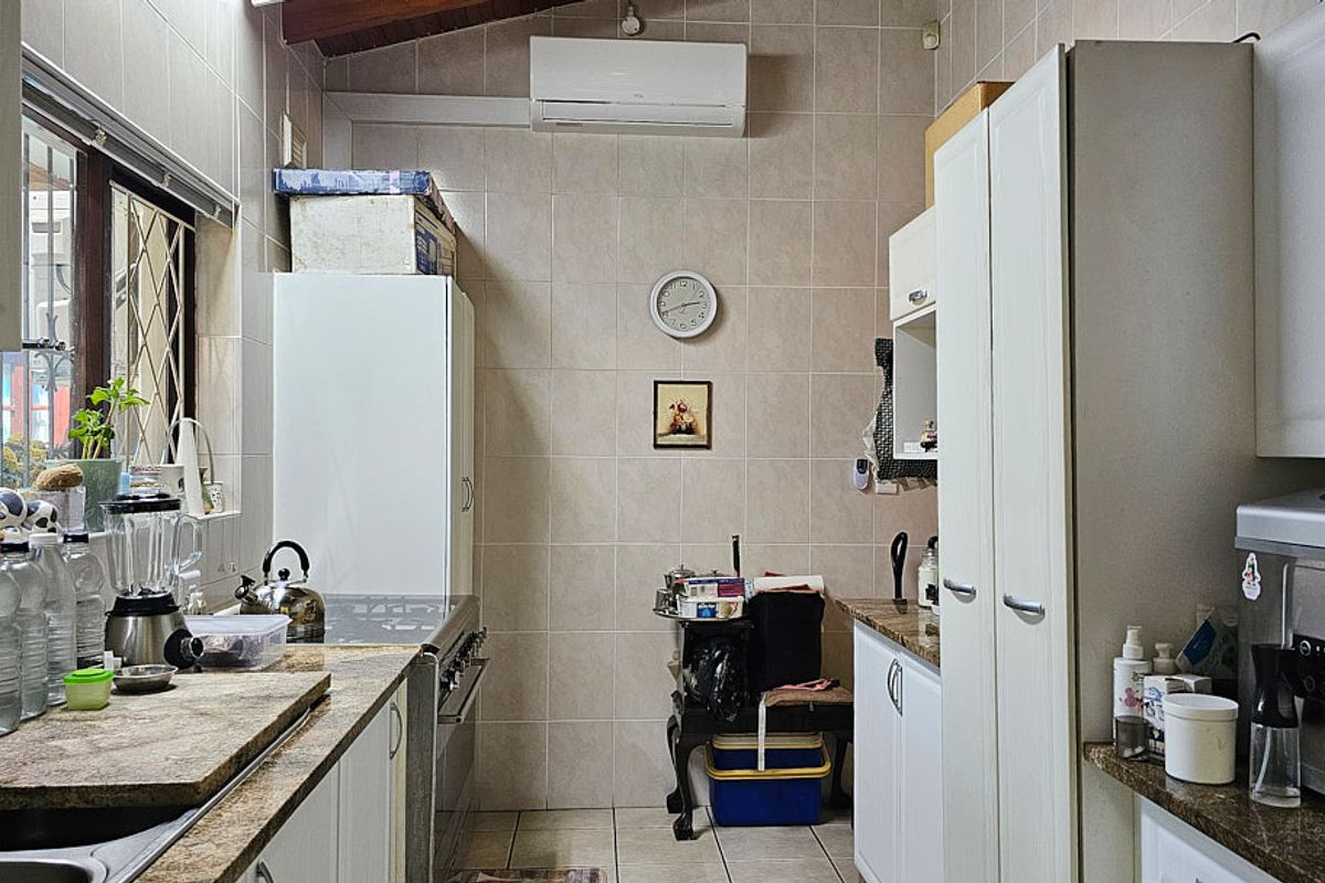 A functional kitchen featuring tiled walls, granite countertops, built-in cabinetry, and a wall-mounted air conditioning unit.