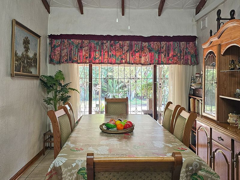 Dining room featuring exposed timber ceiling beams, tiled flooring, and a security gate providing access to the garden area.