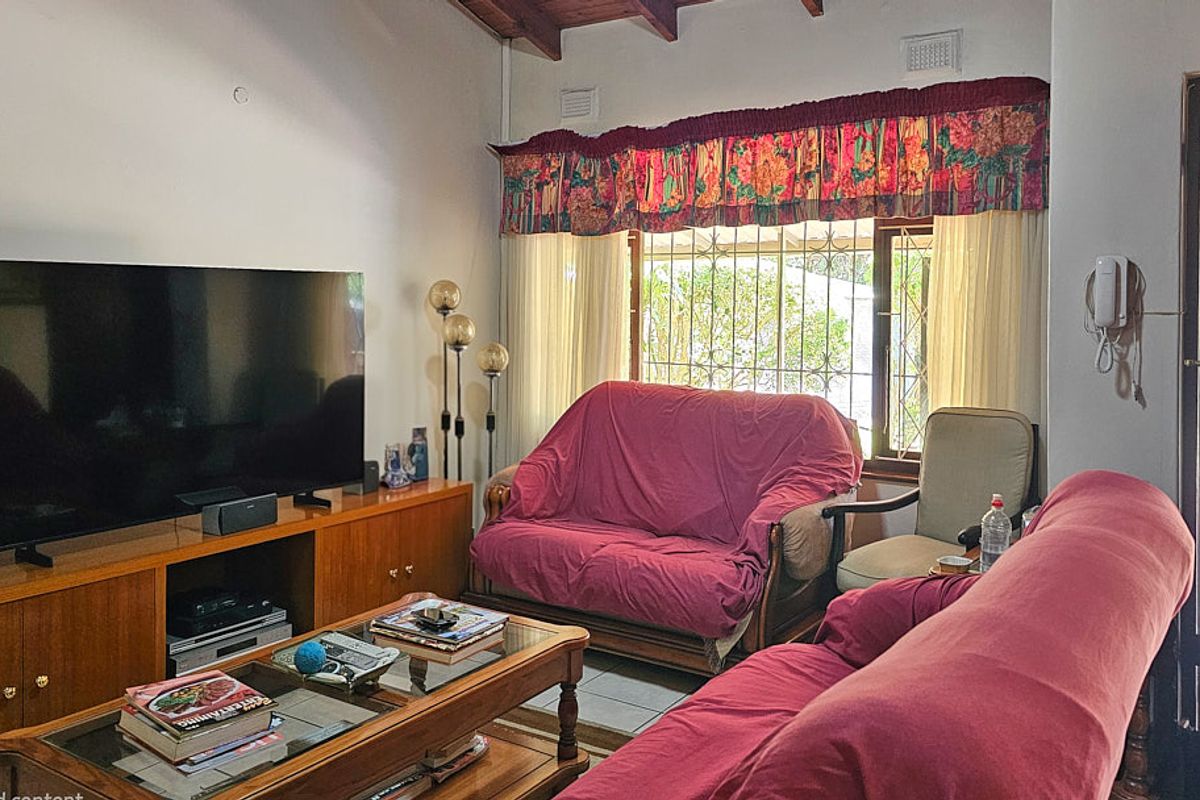 Living room featuring exposed timber ceiling beams, tiled flooring, and security bars on the window, offering direct access to the outdoor area.