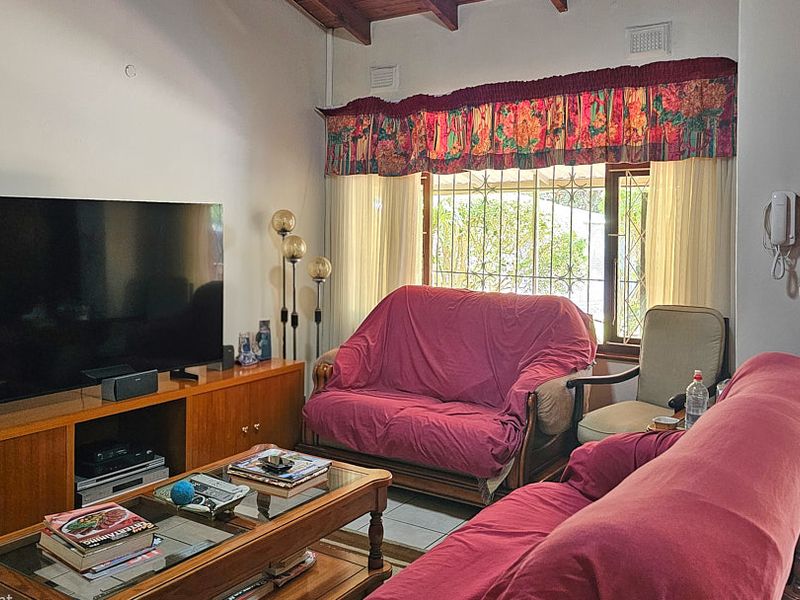 Living room featuring exposed timber ceiling beams, tiled flooring, and security bars on the window, offering direct access to the outdoor area.