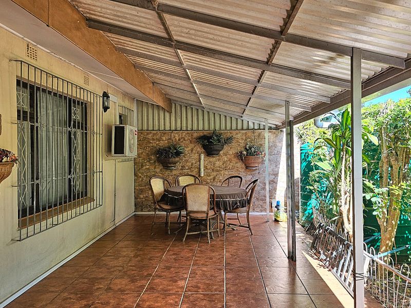 A covered outdoor patio area featuring tiled flooring, stone wall cladding, and security bars on the windows, providing a functional space for outdoor dining.