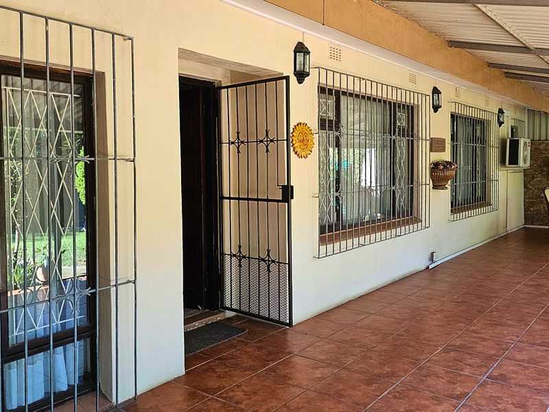 A covered patio area featuring tiled flooring, security bars on windows, and wall-mounted lighting, providing a functional outdoor space for relaxation.