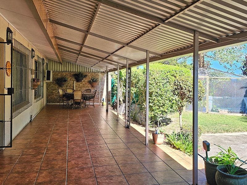 A spacious covered patio featuring tiled flooring and a corrugated metal roof, providing a functional outdoor entertainment area overlooking the garden.