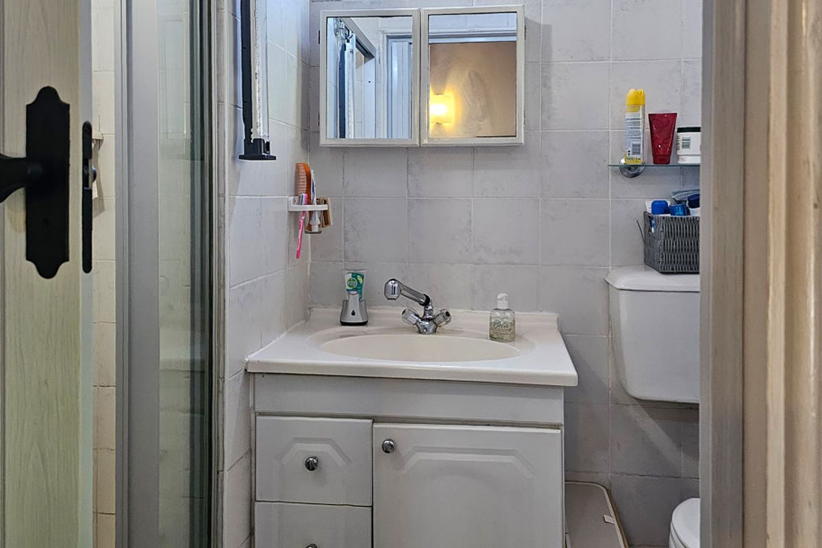 A compact bathroom featuring a vanity unit with integrated basin, a medicine cabinet, a toilet, and a shower enclosure with tiled walls.