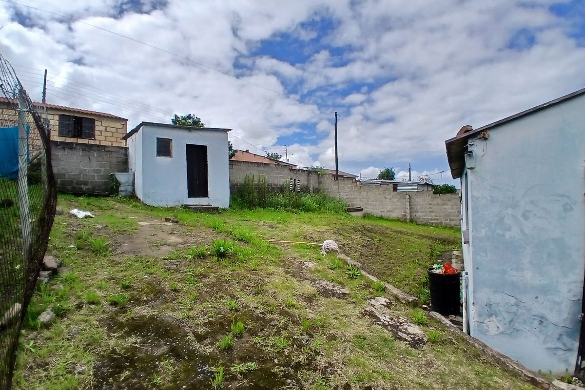 Rear yard area featuring a small outbuilding, concrete block boundary walls, and uneven terrain with natural vegetation.