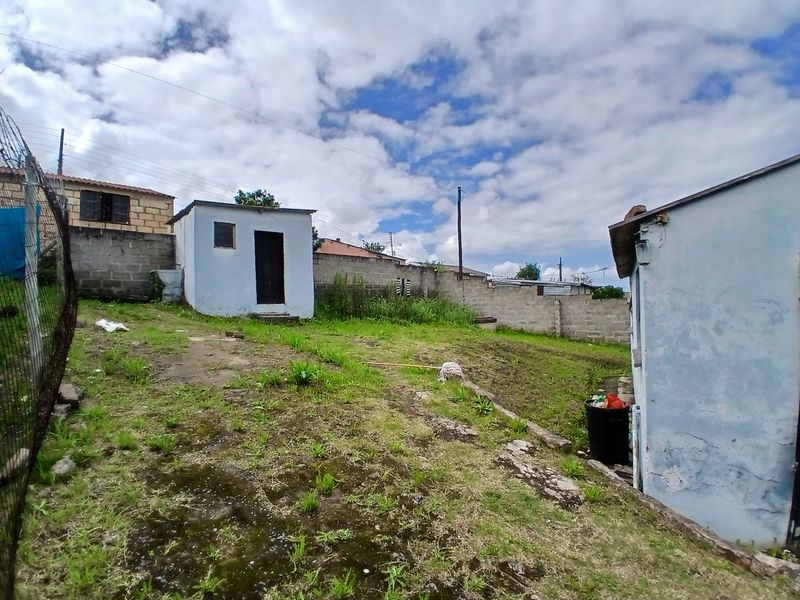 Rear yard area featuring a small outbuilding, concrete block boundary walls, and uneven terrain with natural vegetation.