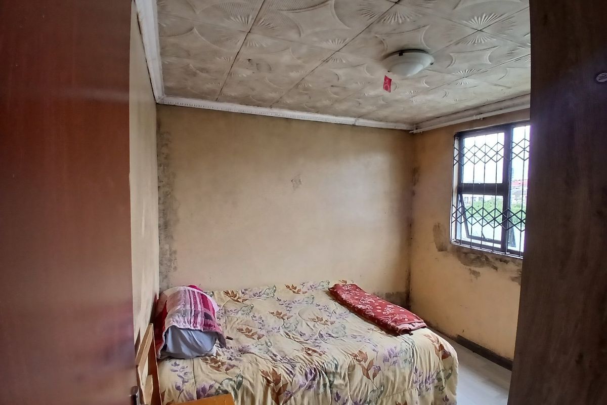 A bedroom featuring decorative ceiling tiles and a window with a security gate, currently showing significant signs of wear and wall damage.