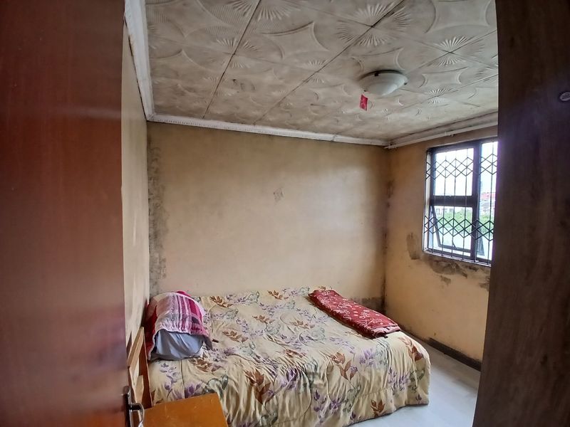 A bedroom featuring decorative ceiling tiles and a window with a security gate, currently showing significant signs of wear and wall damage.