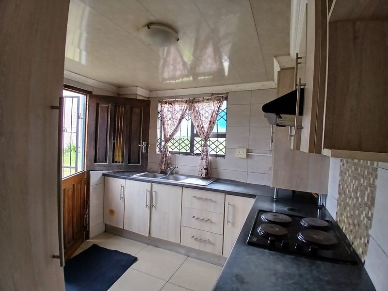 A functional kitchen featuring built-in cabinetry, laminate countertops, a stainless steel sink, and an integrated electric hob with an extractor fan.