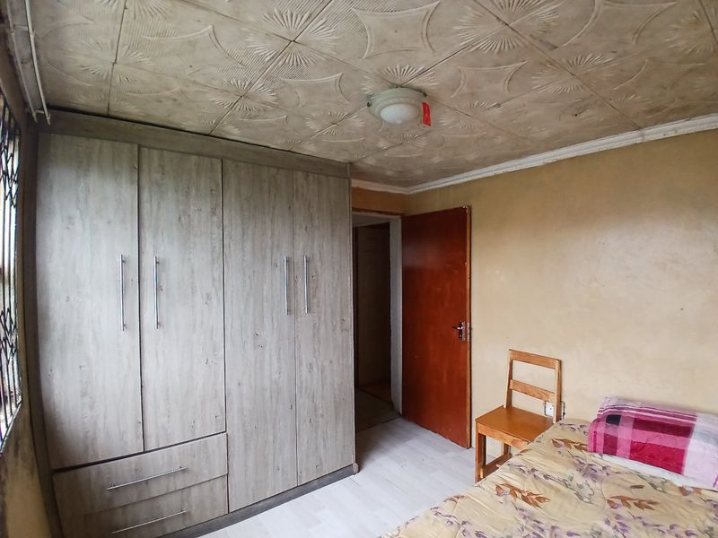 Bedroom featuring a built-in wardrobe, textured ceiling tiles, and laminate flooring. The room requires cosmetic updates to the walls and ceiling.