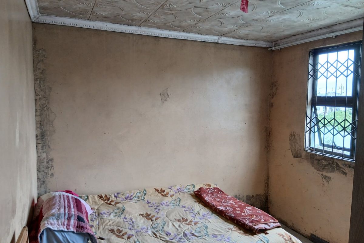 A bedroom featuring decorative ceiling tiles and a security gate on the window, currently requiring significant cosmetic renovation and wall repairs.