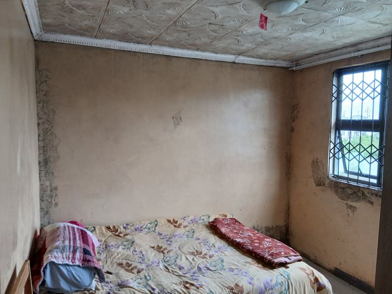 A bedroom featuring decorative ceiling tiles and a security gate on the window, currently requiring significant cosmetic renovation and wall repairs.
