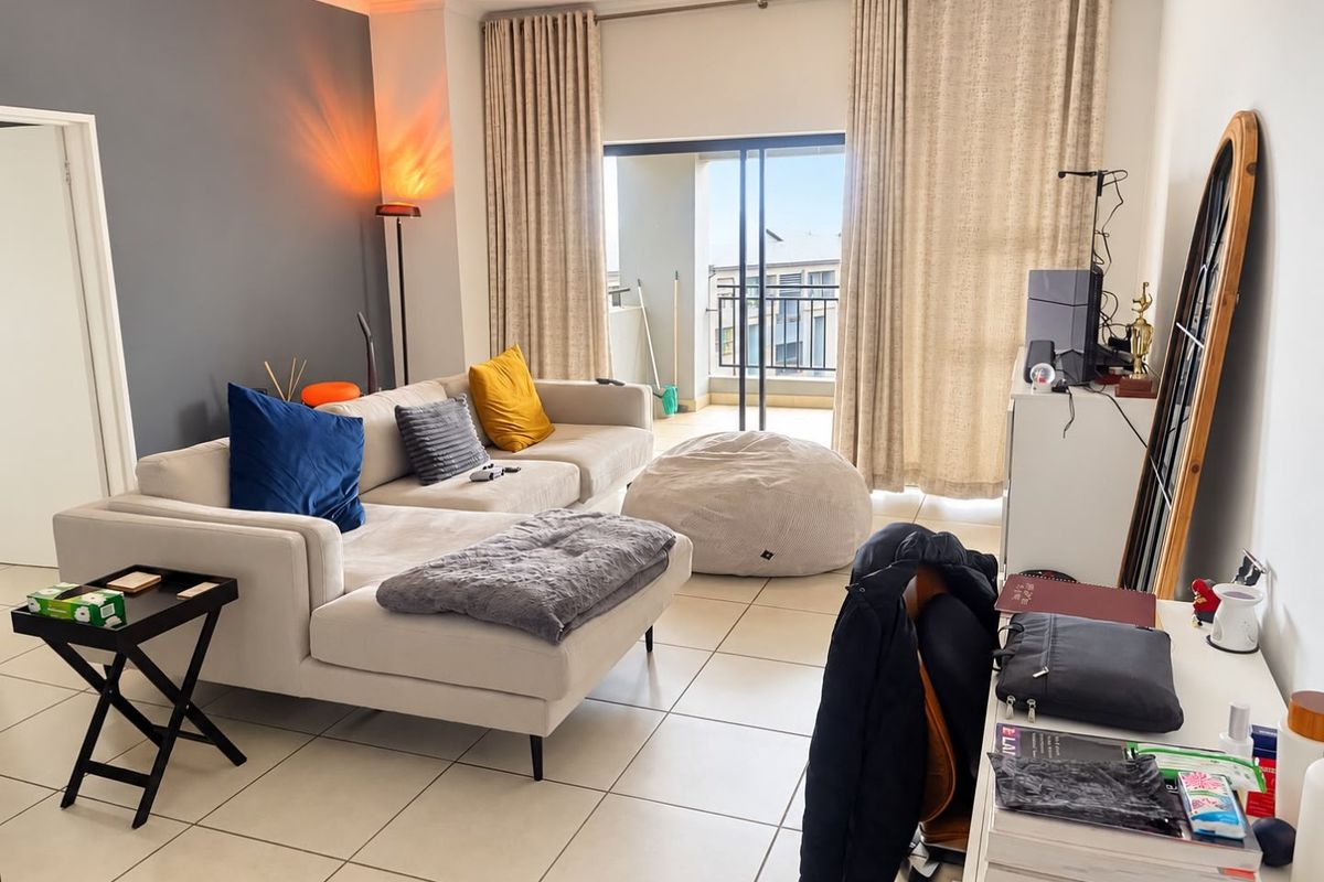 A bright living room featuring tiled flooring and a large sliding glass door providing access to an attached balcony.