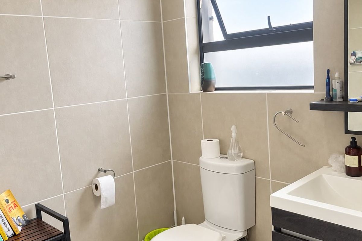 A modern bathroom featuring neutral wall tiles, a wall-mounted vanity, and a top-hung window providing natural light.