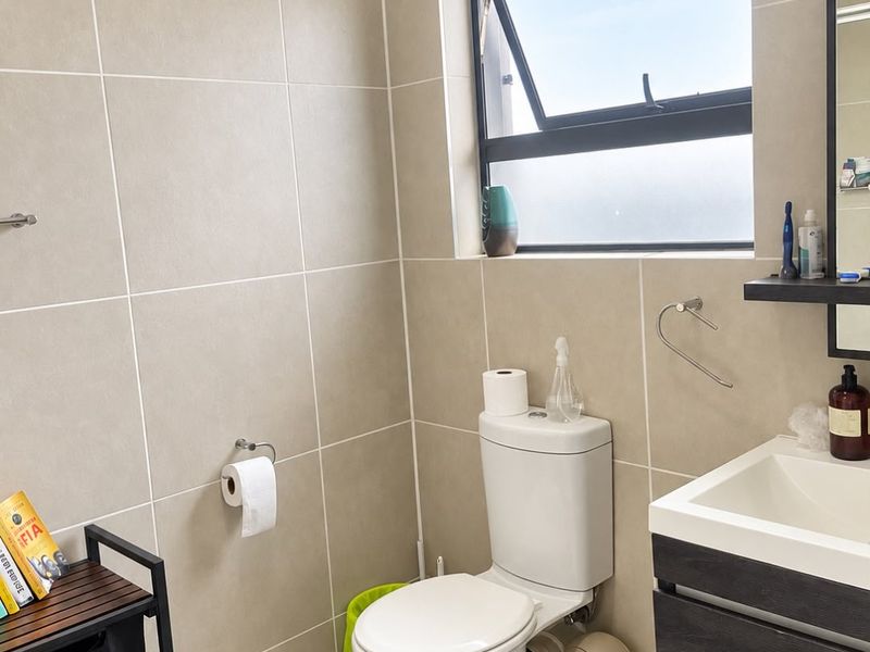 A modern bathroom featuring neutral wall tiles, a wall-mounted vanity, and a top-hung window providing natural light.