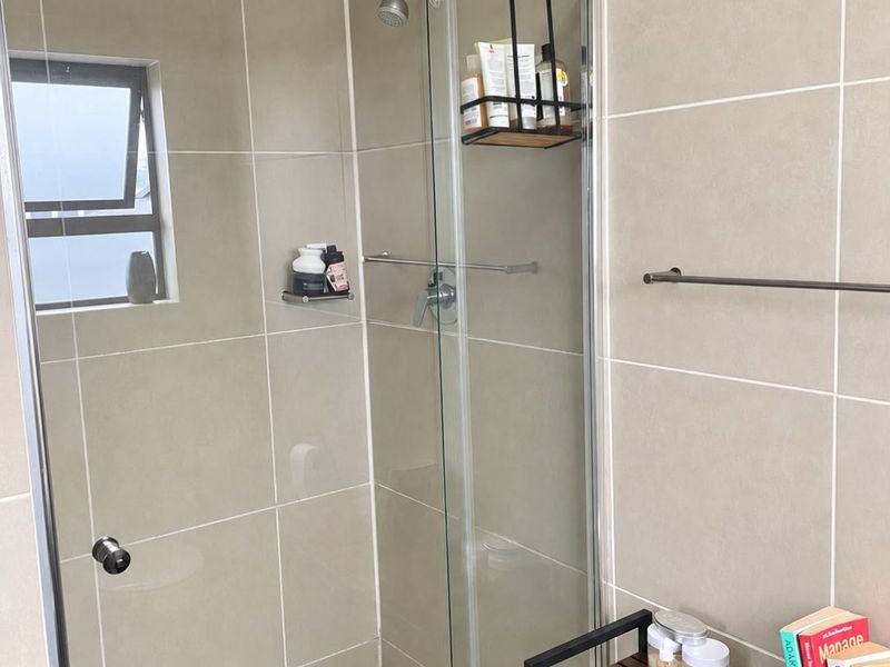 A modern bathroom featuring a glass-enclosed shower with neutral wall tiling and a functional top-hung window for ventilation.