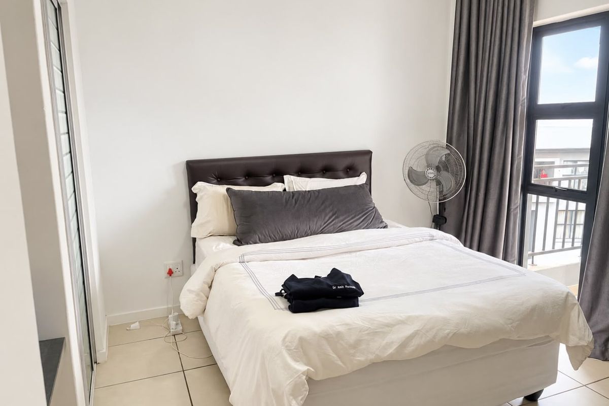 A well-lit bedroom featuring neutral tiled flooring, a built-in cupboard, and a large window with access to a balcony.