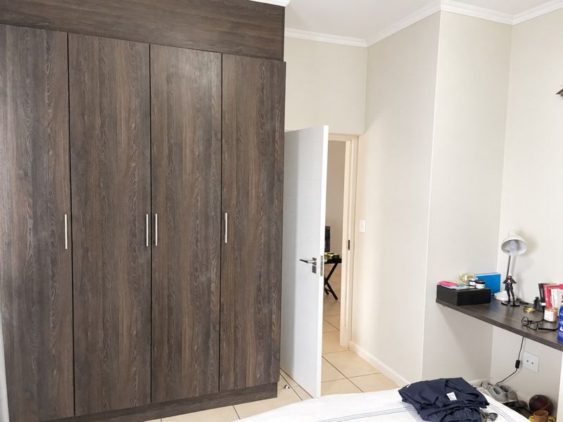 A well-maintained bedroom featuring dark wood-grain built-in wardrobes, tiled flooring, and a convenient built-in desk area.