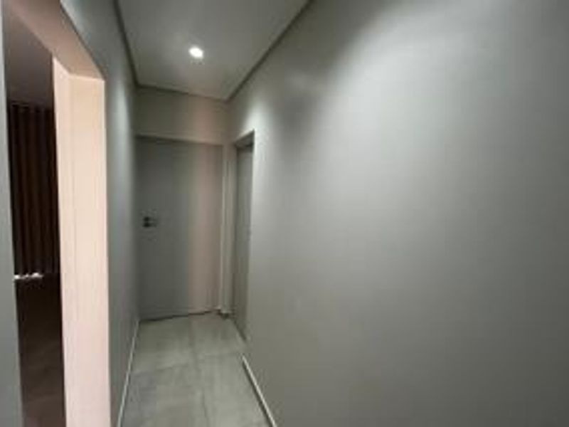 A clean, modern hallway featuring neutral wall finishes, recessed downlighting, and tiled flooring, providing access to adjacent rooms.