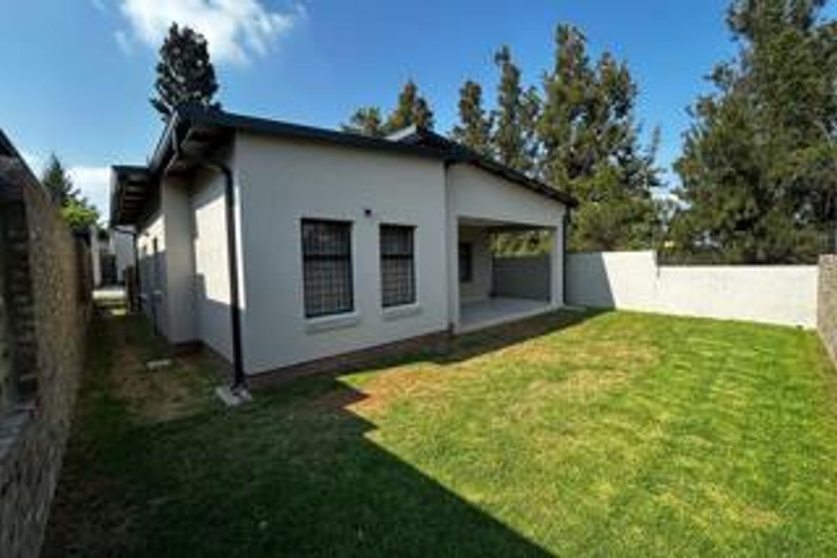 Rear view of the property featuring a covered patio, a well-maintained lawn, and secure boundary walls.