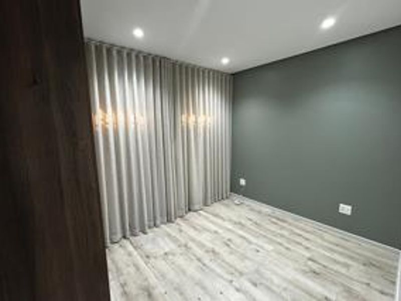A clean, modern bedroom featuring neutral grey walls, light wood-look laminate flooring, and recessed ceiling lighting.