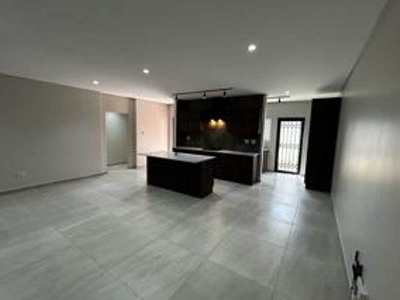 Spacious open-plan living area featuring a modern kitchen with a central island, sleek cabinetry, and neutral tiled flooring throughout.